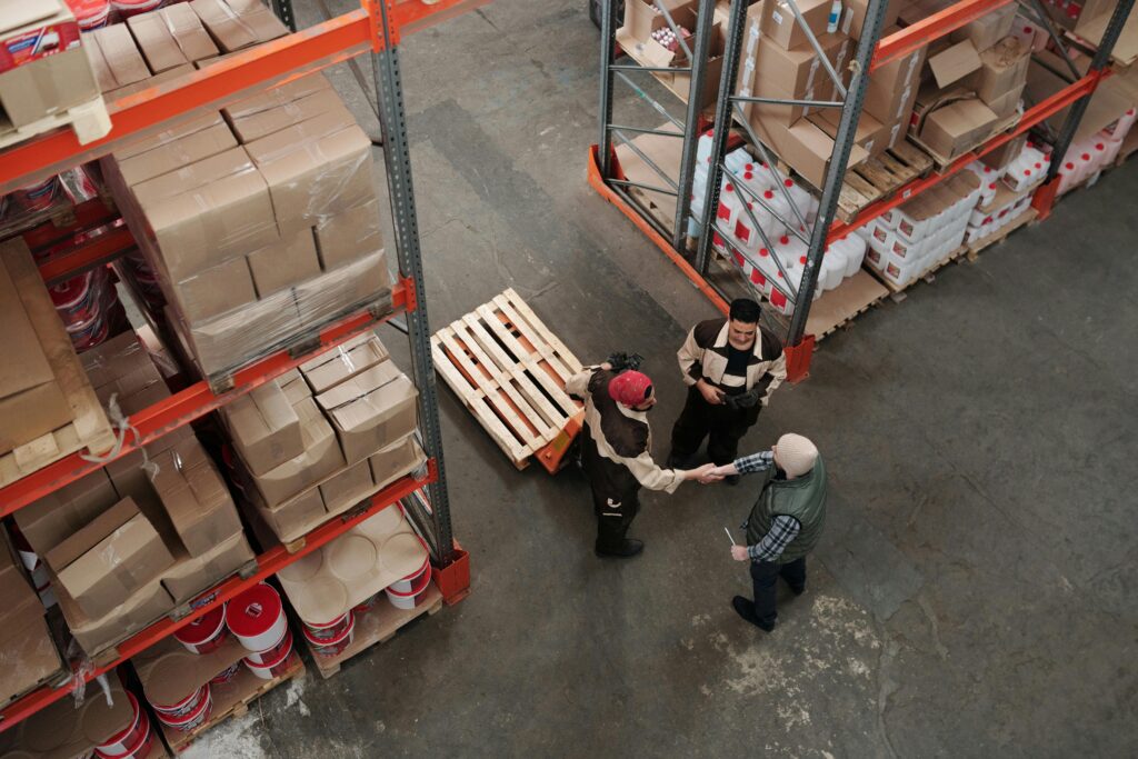 Menu High angle view of workers shaking hands in a warehouse, symbolizing teamwork and logistics.